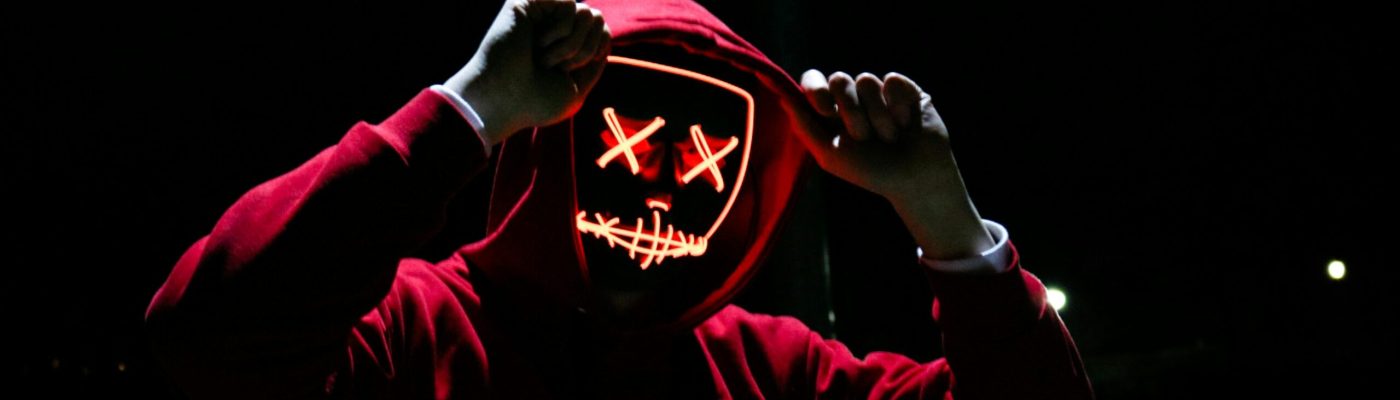 A spooky illuminated mask figure with a red hoodie in a dark setting, perfect for Halloween themes.