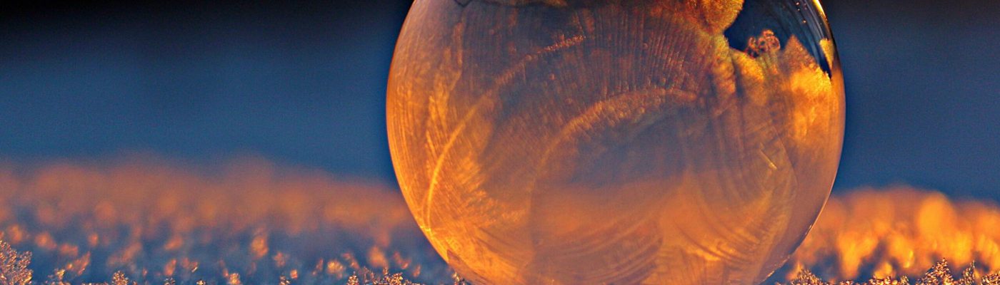 Close-up shot of a frozen bubble with warm reflections resting on a snowy surface at twilight.